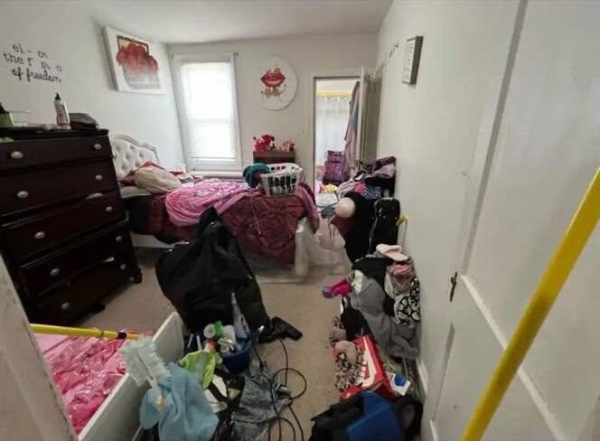 Cluttered bedroom floor covered with clothes, bags, and belongings before cleaning